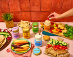 Fabalish dips on a pink table with a spread of vegetables. 
